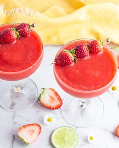 two margaritas with strawberries and lime garnish sit on a marble table