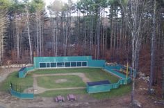 an aerial view of a baseball field in the middle of a forest with benches around it