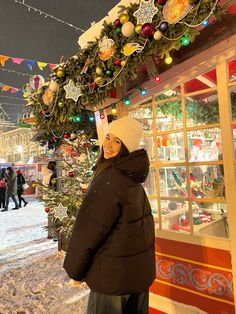 a woman standing in front of a christmas tree with lights and garlands on it