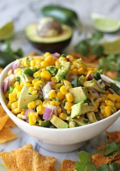 a white bowl filled with corn, avocado and cilantro next to tortilla chips