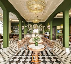 a dining room with green walls and black and white checkered flooring, chandelier above the table