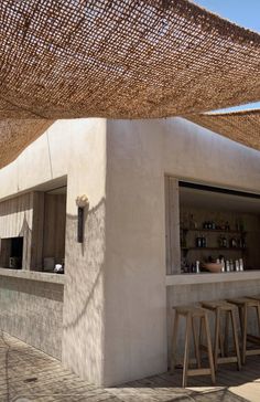 an outdoor bar with several stools under a large shade covering over it's counter area