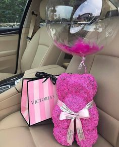 a pink teddy bear sitting in the back seat of a car next to a gift bag