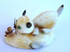 a cat figurine sitting on top of a shell with a snail crawling next to it