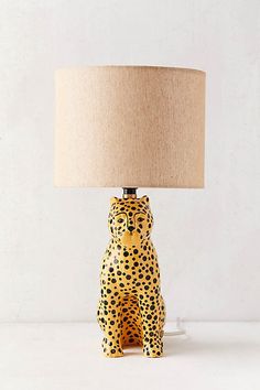 a ceramic leopard lamp with a beige shade on it's head and legs, sitting next to a white wall