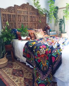 a bed with a colorful blanket and pillows on top of it next to potted plants