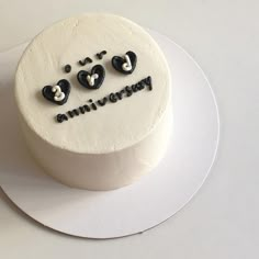 a white cake with black hearts and the words anniversary on it sitting on a plate