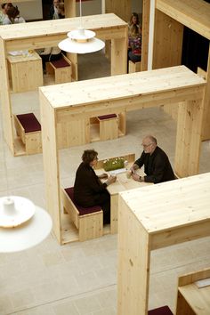 two people are sitting at tables made out of plywood planks in a building