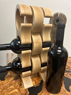 a wine bottle holder made out of wood and black glass bottles on a wooden table