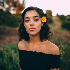 a woman with a yellow flower in her hair is looking at the camera while wearing a black dress