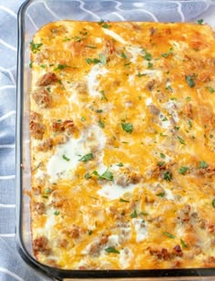 a casserole dish with meat and cheese in it on a blue cloth next to a fork