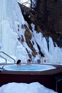 two people are in the hot tub next to an ice - covered waterfall with icicles on it