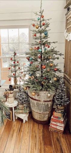 a potted christmas tree with ornaments in it on a wooden floor next to a window