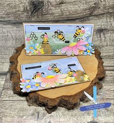 two cards with bees on them sitting on top of a piece of wood next to a pencil