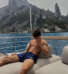 a shirtless man sitting on top of a boat in the ocean next to mountains