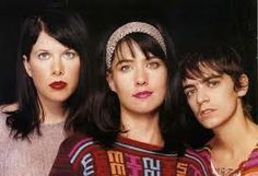 three women standing next to each other in front of a black background with one woman looking at the camera