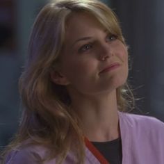 a woman with long blonde hair wearing a purple scrub coat and looking off into the distance