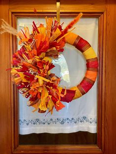 a wreath is hanging on the front door with autumn leaves and feathers attached to it