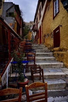 several wooden chairs sitting on the side of a stone street next to steps and buildings