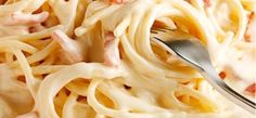 a fork is stuck into some pasta with bacon and cream sauce on the top,