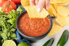 a hand dipping a tortilla chip into a bowl of salsa