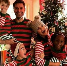 a group of people in matching christmas sweaters standing next to a christmas tree and smiling