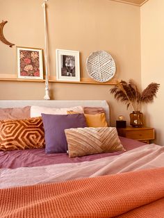 a bed with purple and orange pillows in a bedroom next to pictures on the wall