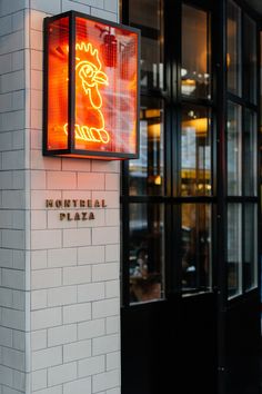 a neon sign on the side of a building in front of a restaurant with people walking by