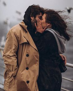 a man and woman kissing while standing next to each other on a bridge over looking the water