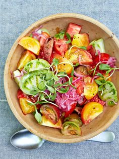 a wooden bowl filled with lots of different types of vegetables next to two spoons