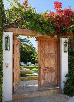 two wooden doors are open in front of a white building with flowers growing on it