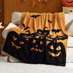 a black and orange blanket with pumpkins on it in front of a white couch