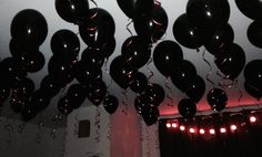 many black balloons are hanging from the ceiling in a room with red lights and curtains