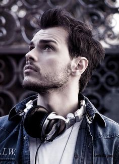 a man with headphones standing in front of a fence and looking off into the distance