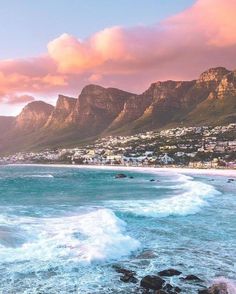 the ocean with waves crashing in front of some mountains and houses on the other side