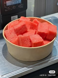 a bowl filled with watermelon sitting on top of a counter next to a digital clock