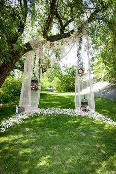 an outdoor ceremony setup with white flowers on the grass and hanging lanterns in the trees