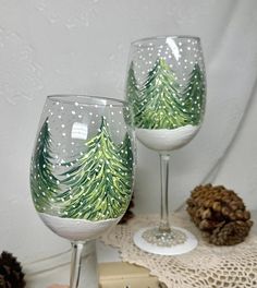 two wine glasses sitting on top of a table next to pine cones and christmas decorations