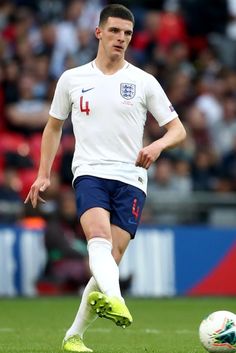 a man in white shirt and blue shorts kicking a soccer ball on field with crowd watching