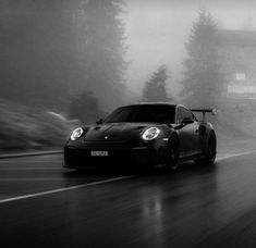 a black and white photo of a sports car driving on a road in the rain