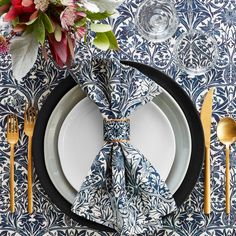 a place setting with blue and white plates, silverware and flowers on the table