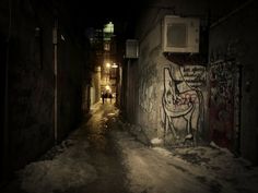 a dark alley with graffiti on the walls and one person walking down it at night