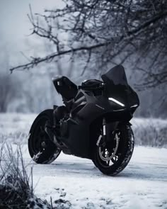 a black motorcycle parked on the side of a snow covered road next to a tree