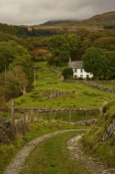 a small white house sitting on the side of a lush green hillside next to a dirt road