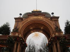 an archway with christmas lights and decorations on the sides is lit up in front of trees