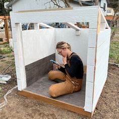 a woman sitting on the ground using a cell phone in a small building with wood flooring