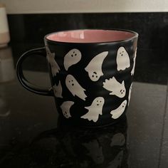 a black and white mug with ghost faces on it sitting on top of a counter