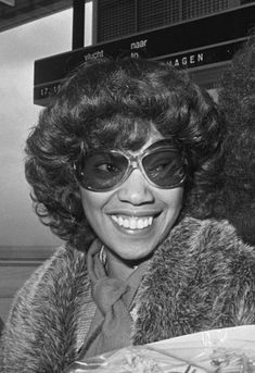 an old photo of two women in sunglasses and fur coats smiling at the camera while holding a plate of food