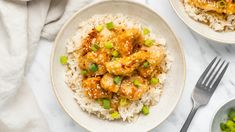 two plates filled with chicken and rice on top of a white table cloth next to silverware