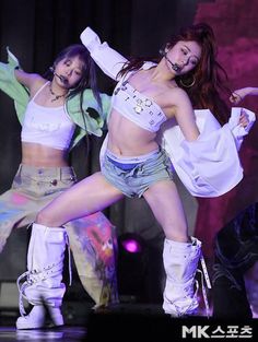 two women in short shorts and boots on stage with one holding her leg up to the side